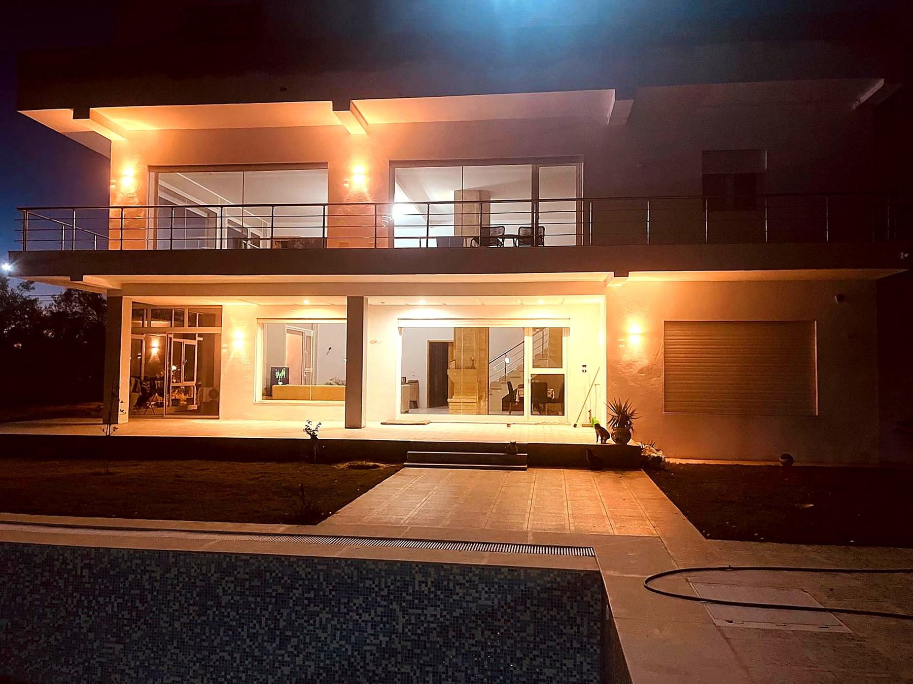Villa facade illuminated at night with pool in foreground
